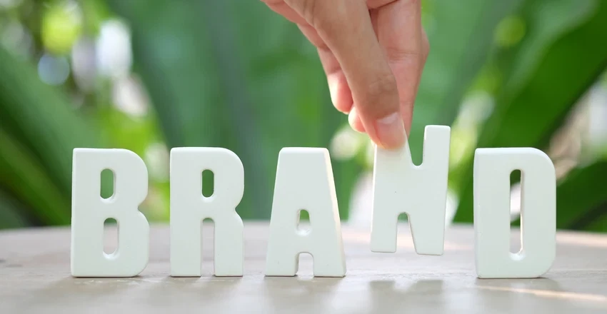 A hand arranging wooden letter tiles that spell out BRAND.