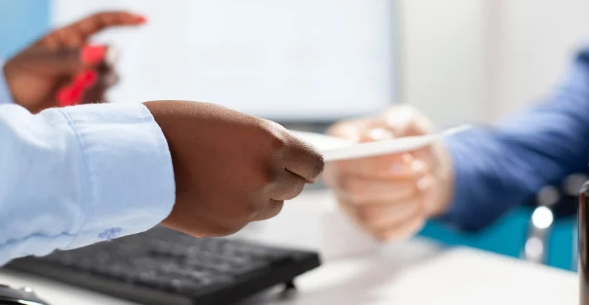 Close-up of two people's hands exchanging a signed document across a desk.